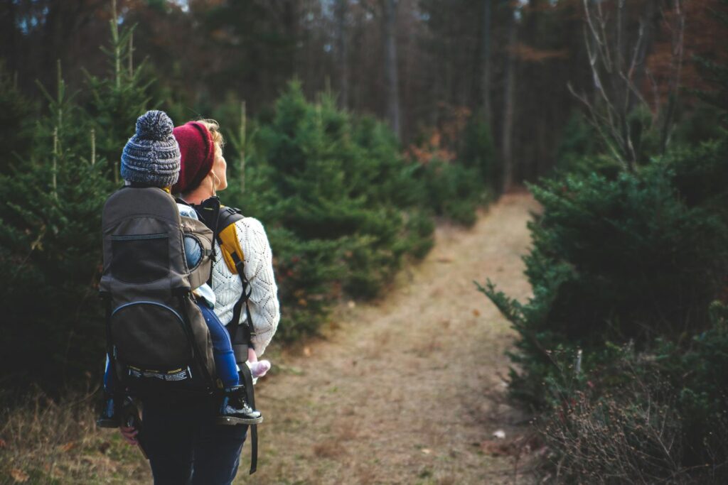 A mother with her child in a carrier backpack hiking through a forest trail on a crisp autumn day.